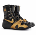 A pair of Nike high-top boxing shoes in black and gold, featuring a patterned upper, gold Swoosh logo, and gold hook-and-loop strap closure, shown on a white background.